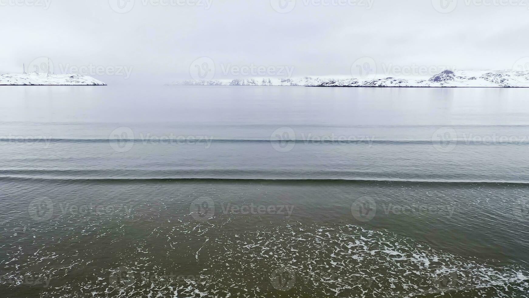 top visie van zee Aan achtergrond van kust in winter. filmmateriaal. mooi winter panorama van stil blauw zee Aan achtergrond van besneeuwd kust foto