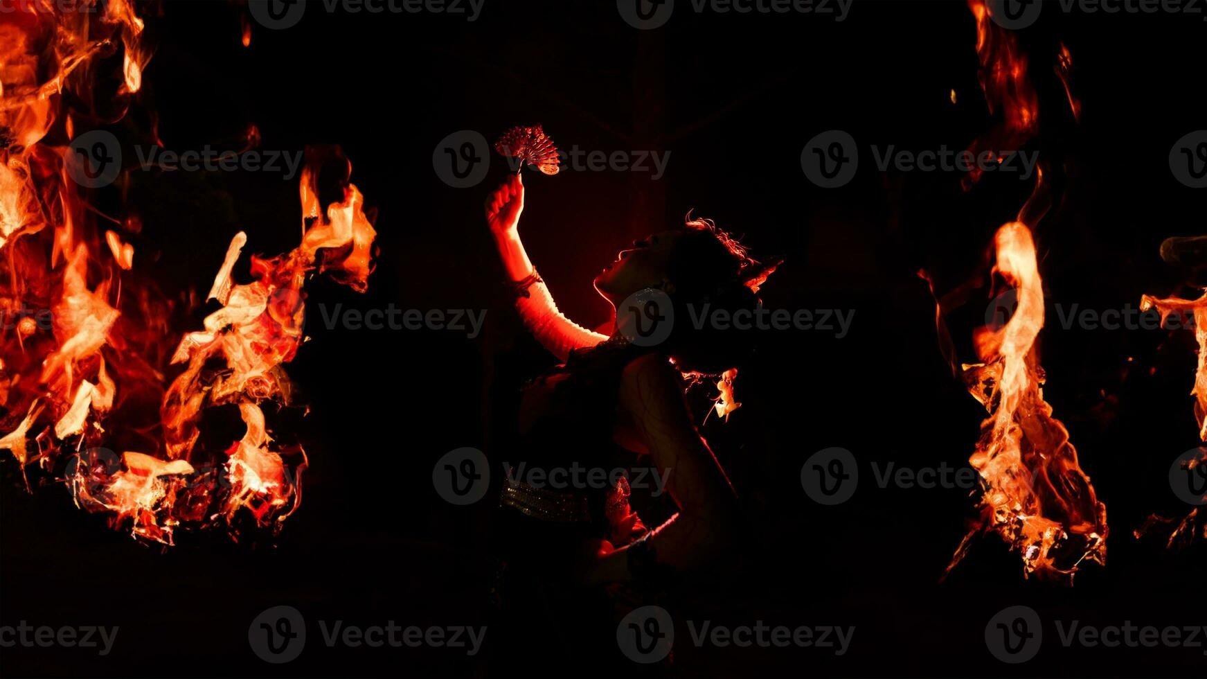 de silhouet van een vrouw danser Holding sieraden in de donker van nacht is lit door de licht van een brandend brand foto