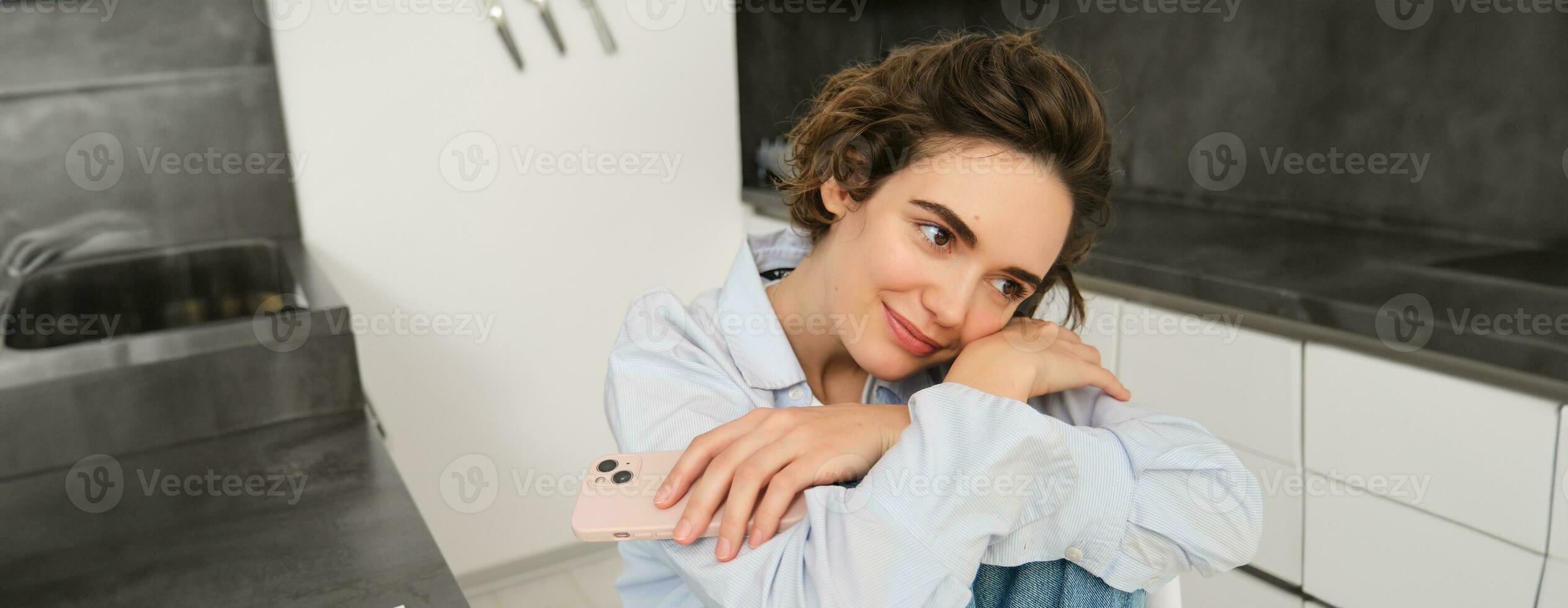 dichtbij omhoog portret van dromerig, mooi vrouw denken van iets Vrolijk, Holding smartphone, aan het wachten voor een bericht of telefoon telefoongesprek, uitgeven tijd Bij huis foto