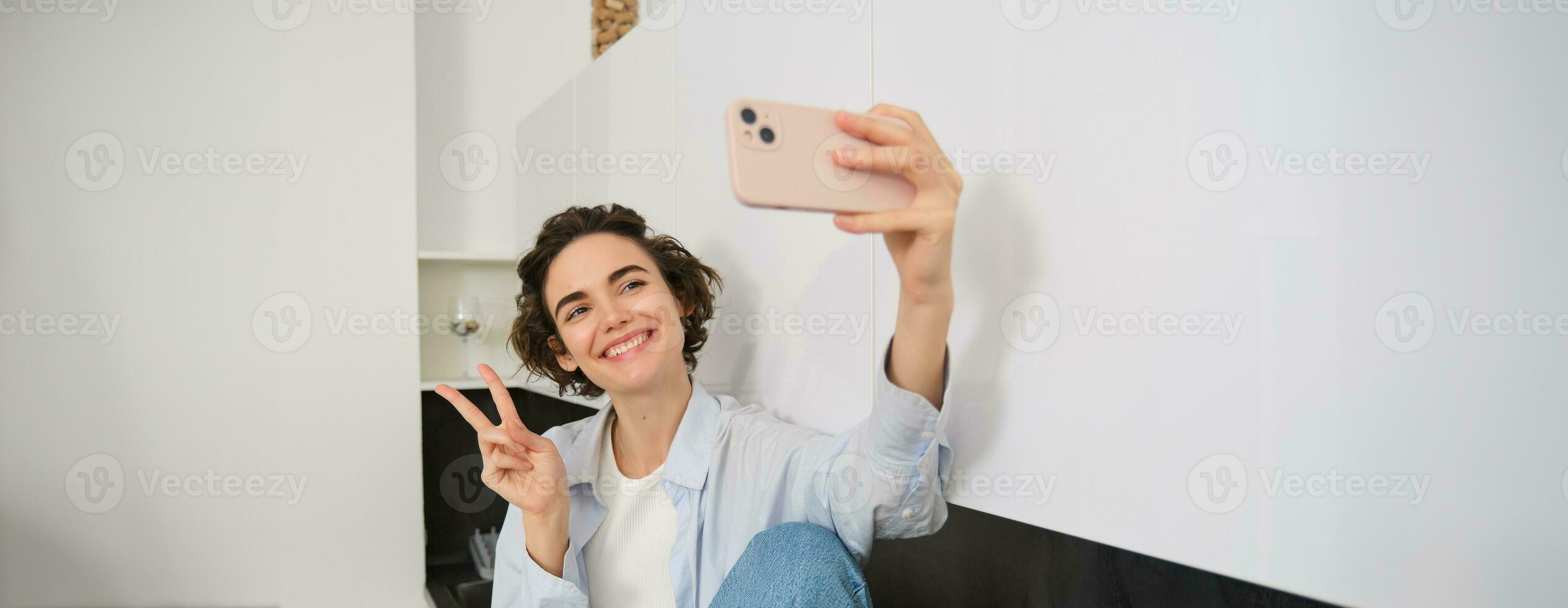 portret van mooi brunette meisje, duurt selfie Aan smartphone in haar keuken, poseren voor foto Aan mobiel telefoon