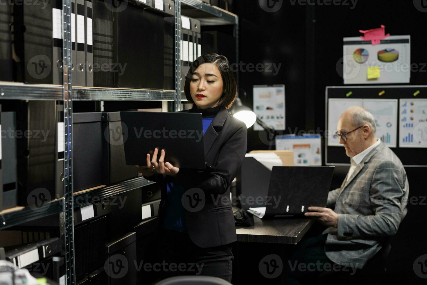 Aziatisch privaat onderzoeker in agentschap bewaarplaats kantoor kamer op zoek voor crimineel geval het dossier papierwerk Aan kabinet planken. detective vrouw en ouderen assistent collega omringd door criminologie mappen foto