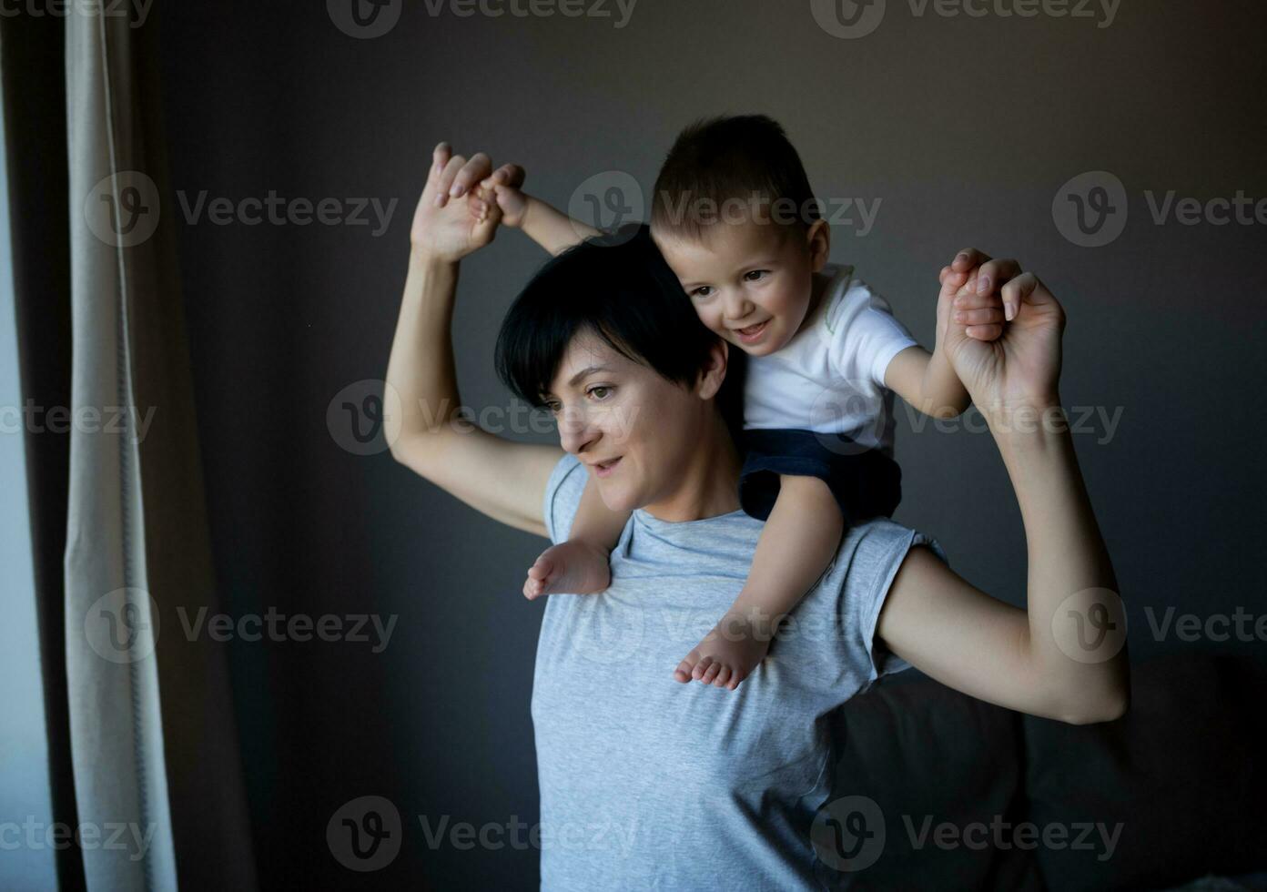een jong vrouw is Holding haar weinig zoon Aan haar schouders. familie portret foto