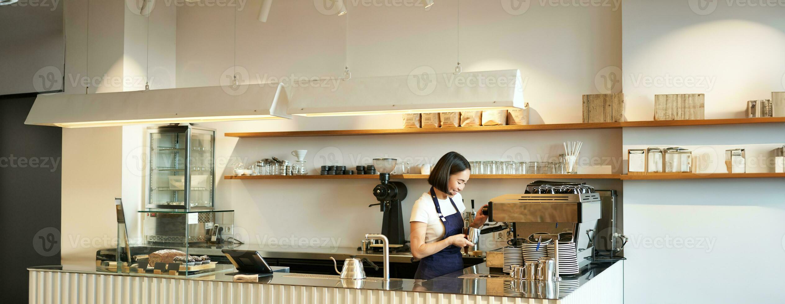 portret van cafe teller met barista meisje werken met koffie machine, maken bestellen voor cliënt in winkel, vervelend blauw schort foto