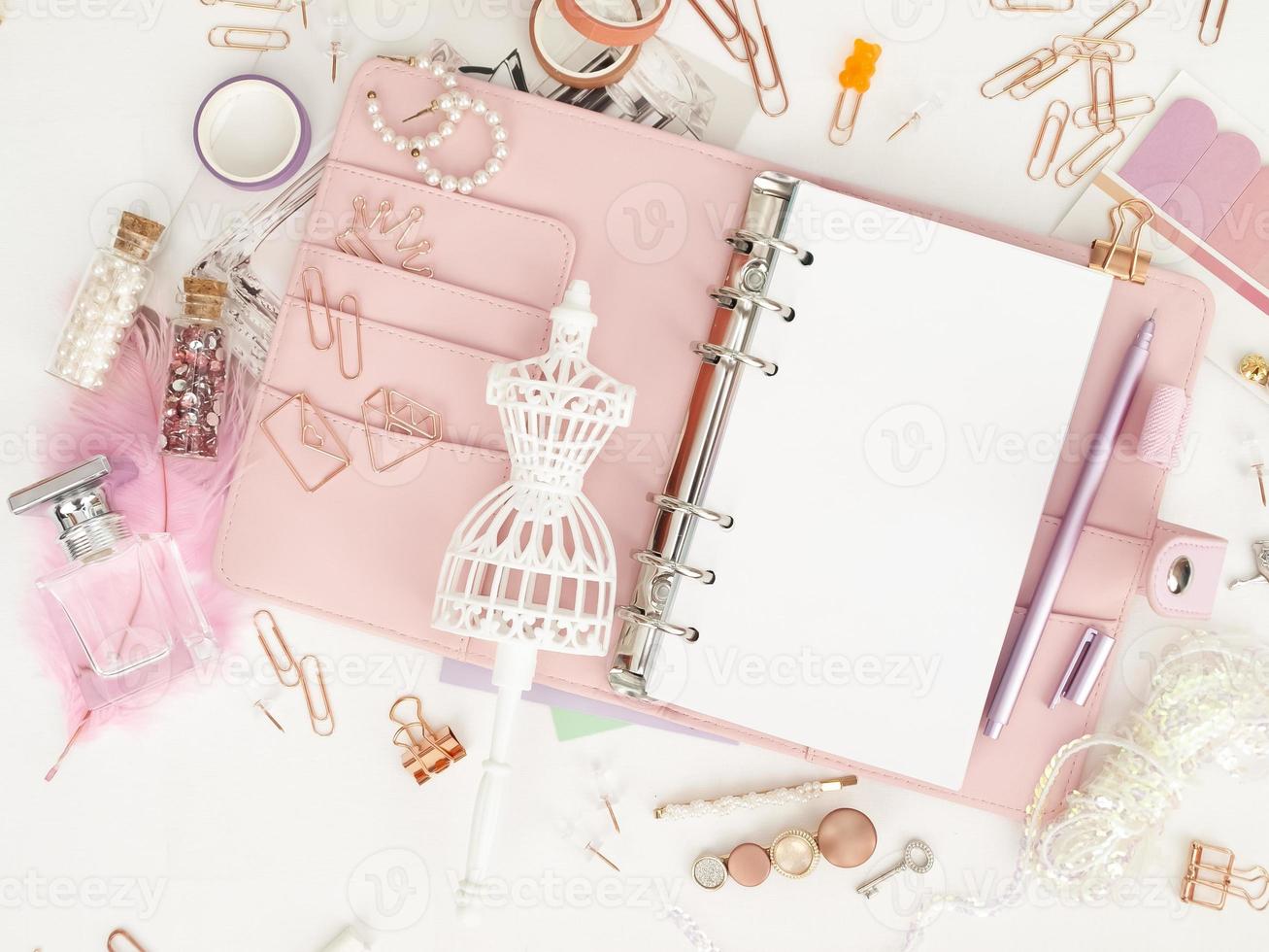 bovenaanzicht van een roze planner met schattig briefpapier. roze glamourplanner met een wit paspopbeeldje. planner met open pagina's op een witte achtergrond en met mooie accessoires pennen, knopen, pinnen. foto