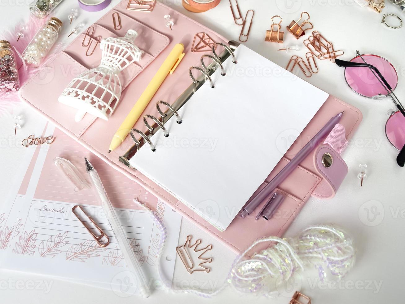 bovenaanzicht van een roze planner met schattig briefpapier. roze glamourplanner met een wit paspopbeeldje. planner met open pagina's op een witte achtergrond en met mooie accessoires pennen, knopen, pinnen. foto