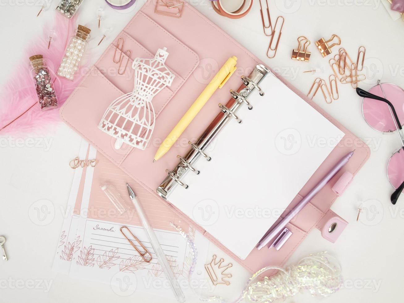 bovenaanzicht van een roze planner met schattig briefpapier. roze glamourplanner met een wit paspopbeeldje. planner met open pagina's op een witte achtergrond en met mooie accessoires pennen, knopen, pinnen. foto