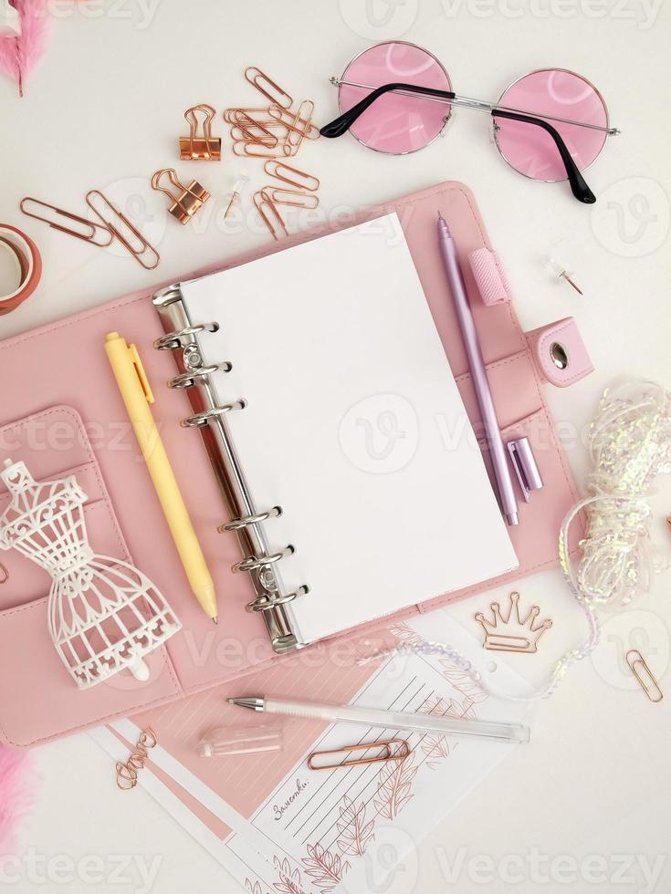 bovenaanzicht van een roze planner met schattig briefpapier. roze glamourplanner met een wit paspopbeeldje. planner met open pagina's op een witte achtergrond en met mooie accessoires pennen, knopen, pinnen. foto