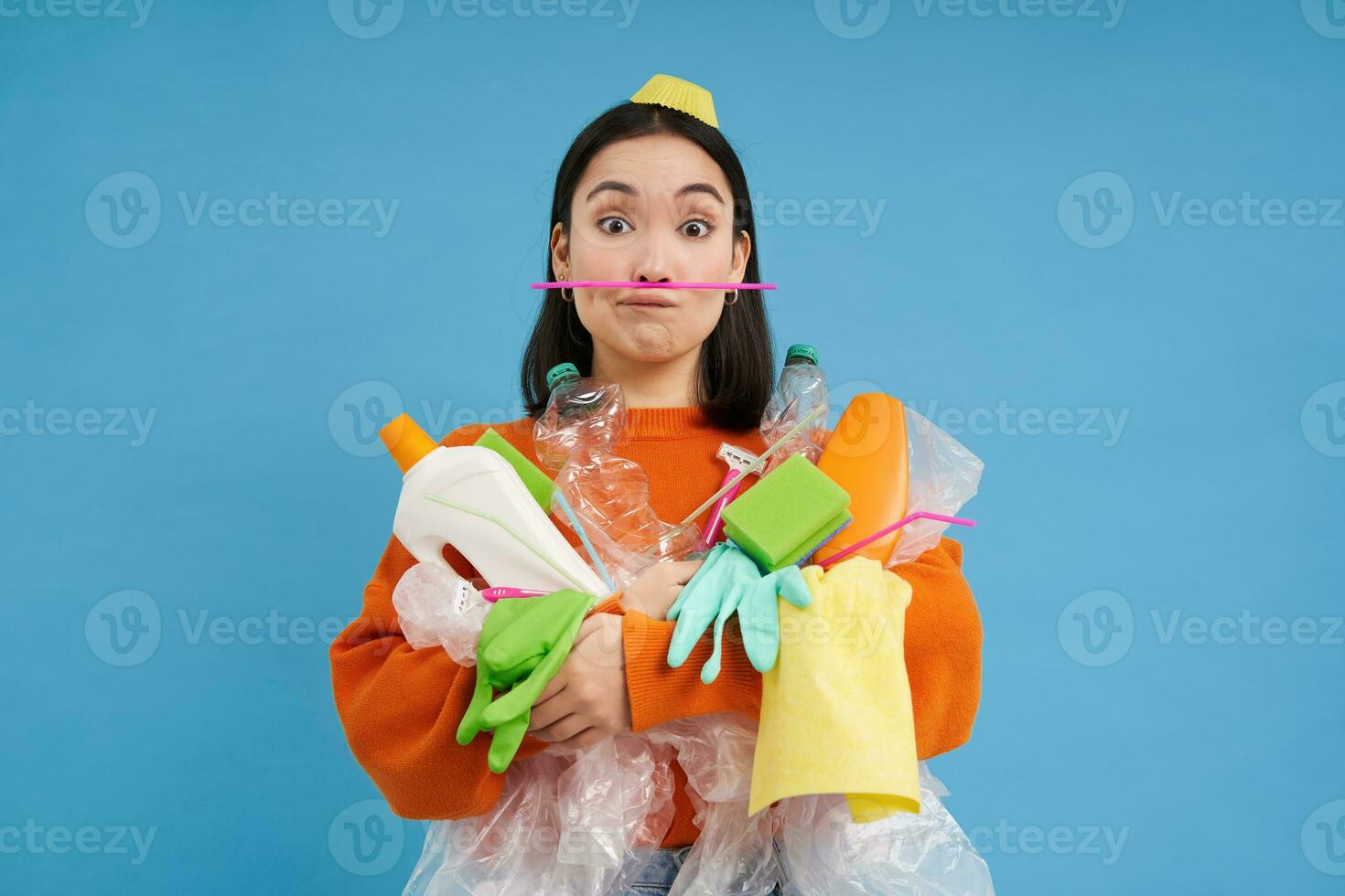 grappig Aziatisch vrouw Holding plastic vuilnis en maakt gezichten, verzamelen verspilling voor recycling centrum, blauw achtergrond foto