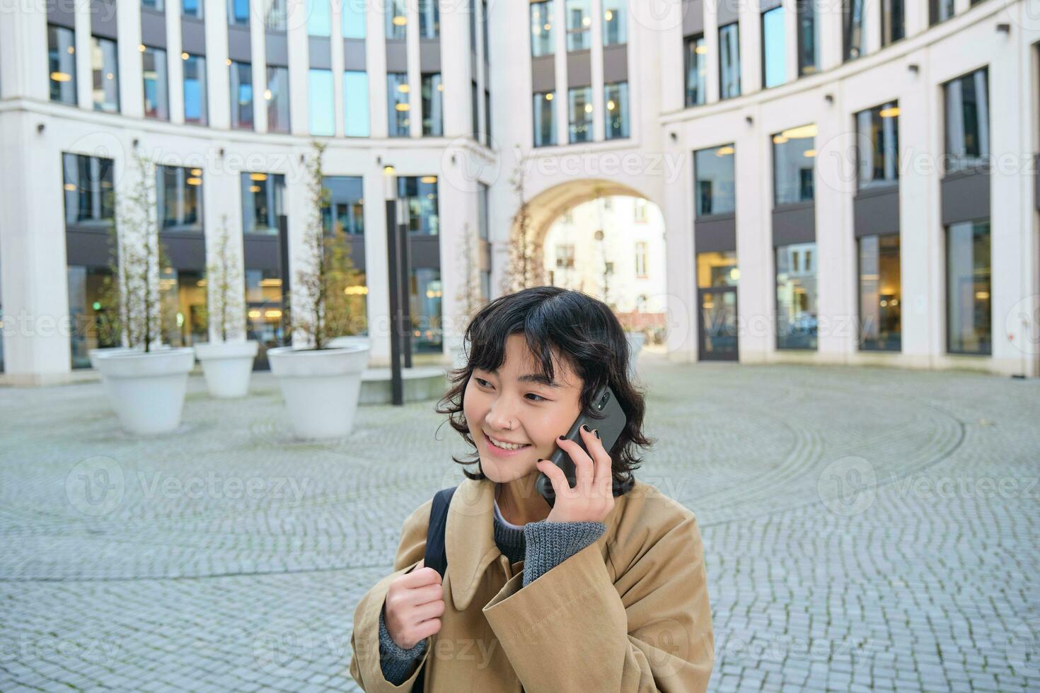 cellulair technologie. jong Koreaans vrouw praat Aan mobiel telefoon, maakt een telefoon telefoontje Aan haar manier huis, wandelingen naar beneden straat, stad centrum, heeft telefoon gesprek foto