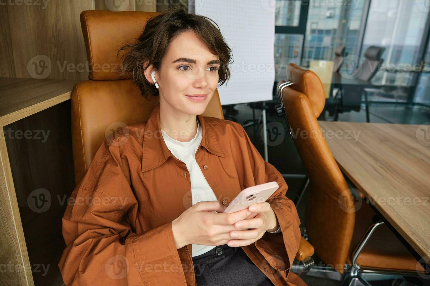 portret van vrouw werken in een kantoor, werknemer gebruik makend van smartphone, zittend in stoel Aan haar breken en glimlachen foto