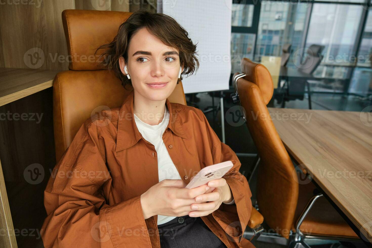 portret van verkoopster in kantoor, begin omhoog werknemer met smartphone, zittend in stoel, luisteren muziek- in draadloze hoofdtelefoons foto