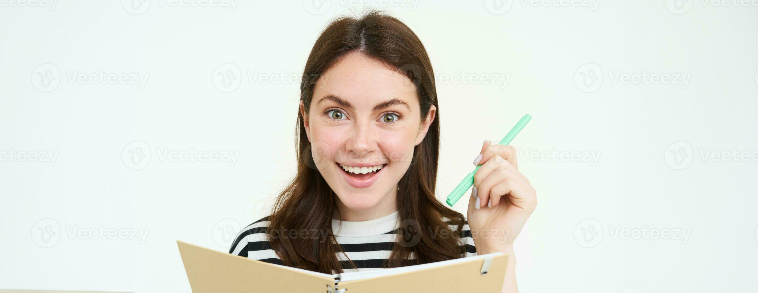 portret van mooi, glimlachen jong vrouw, Holding pen en notitieboekje, op zoek gelukkig Bij camera, maken notities, schrijven in planner, staand over- wit achtergrond foto