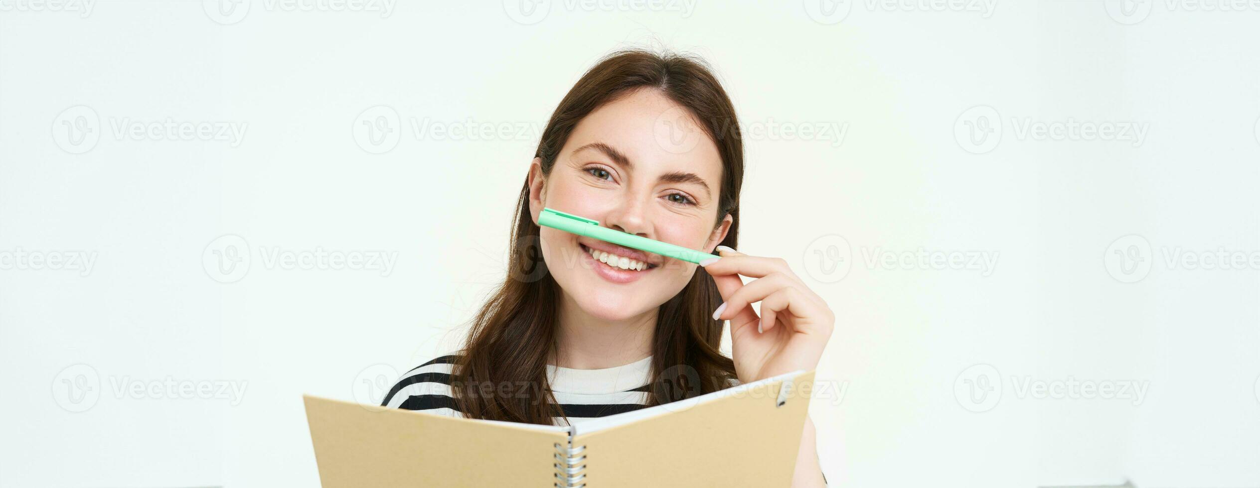 portret van grappig, glimlachen vrouw met notitieboekje, Holding pen De volgende naar haar lip en op zoek Vrolijk, wit achtergrond foto