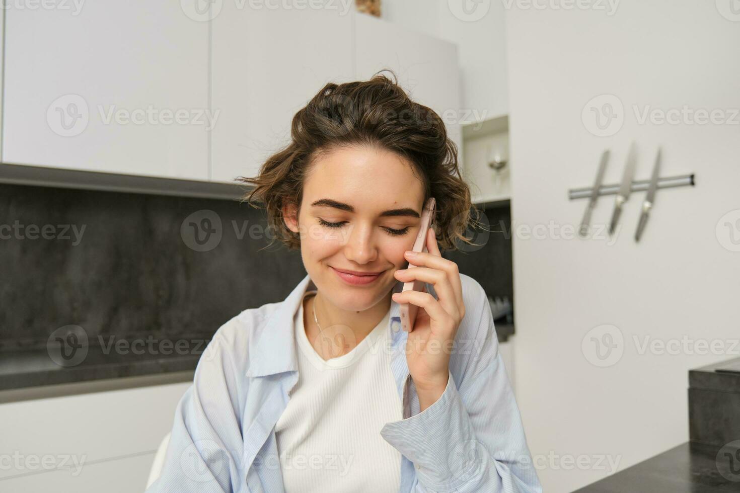 portret van mooi meisje praat Aan mobiel telefoon, heeft gesprek, antwoord een telefoontje in keuken foto