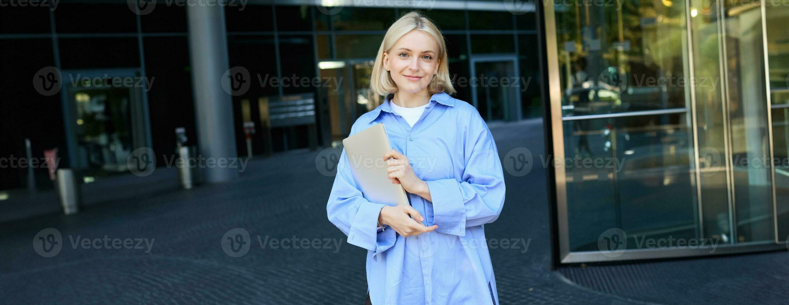 beeld van jong vrouw medewerker, werken vrouw staand in de buurt haar kantoor Aan straat, Holding stapel van documenten en glimlachen foto