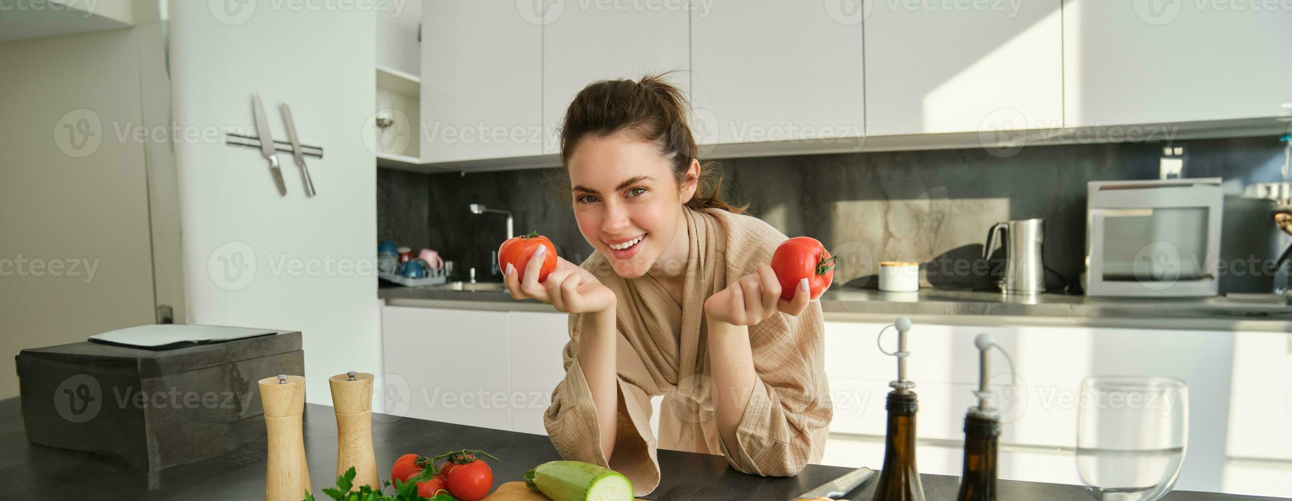 portret van vrouw Koken Bij huis in de keuken, Holding tomaten, voorbereidingen treffen heerlijk vers maaltijd met groenten, staand in de buurt hakken bord foto