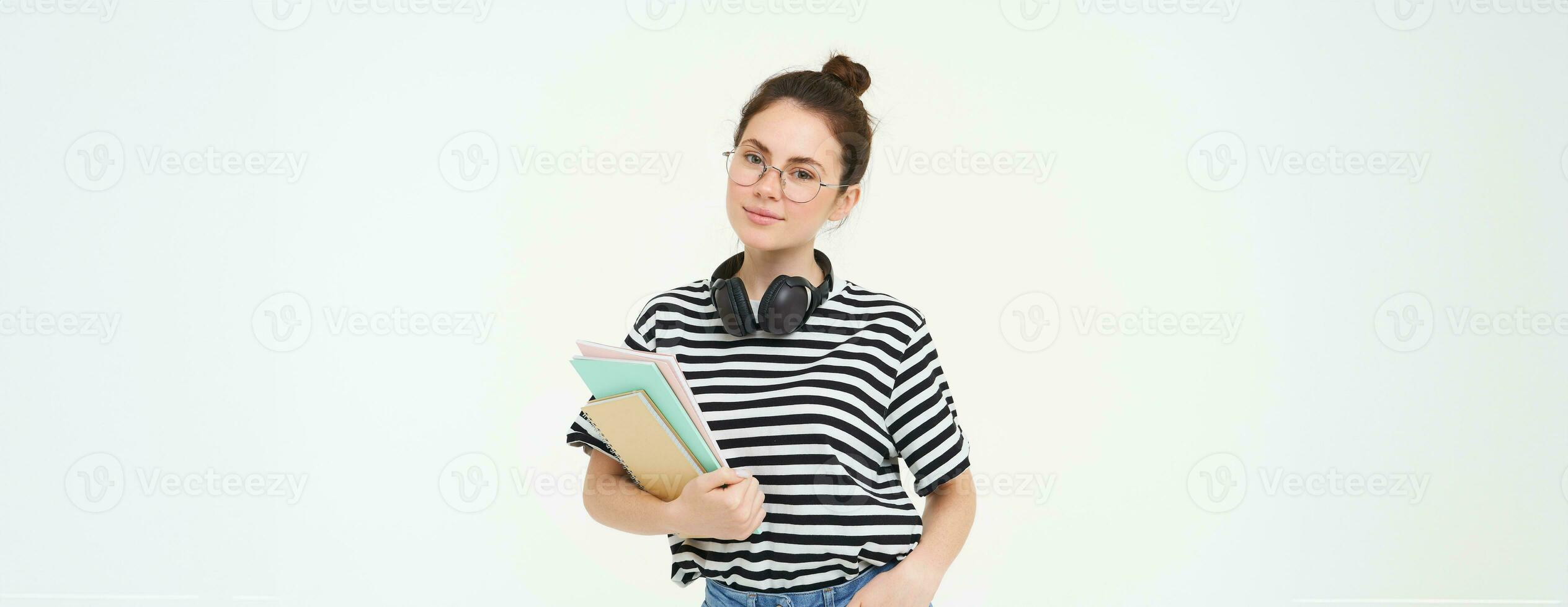 onderwijs concept. glimlachen brunette meisje, leerling in gewoontjes kleren, houdt haar boeken, studie materiaal, draagt hoofdtelefoons over- nek, looks zelfverzekerd en Vrolijk, geïsoleerd over- wit achtergrond foto