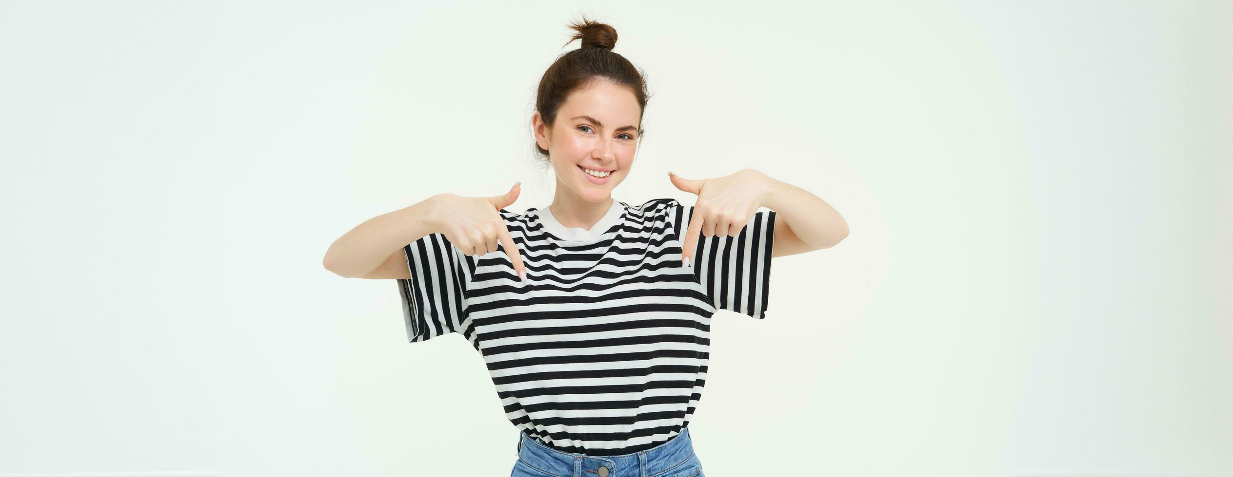 portret van lachend, mooi jong vrouw, richten vingers omlaag, tonen advertentie, poseren tegen wit achtergrond foto