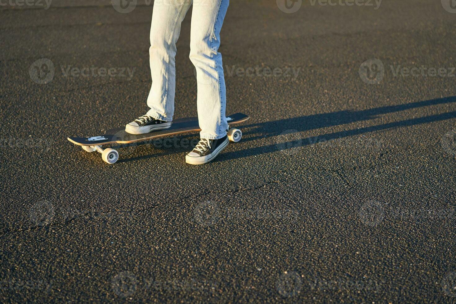 bijgesneden schot van poten Aan longboard. schaatser meisje rijden haar skateboard Aan straat. vrouw tiener Aan kruiser foto