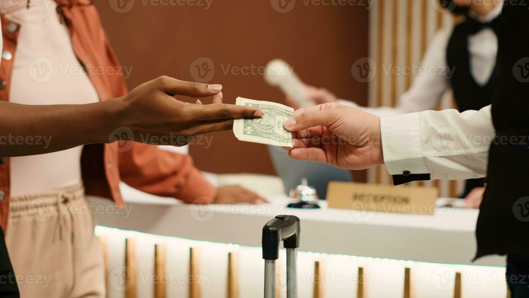 dichtbij omhoog van Afrikaanse Amerikaans vrouw overhandigen dollar bankbiljet naar piccolo werknemer na ontvangen Super goed klant onderhoud. dankbaar toerist fooien nuttig portier voor helpen met bagage in hotel lobby foto