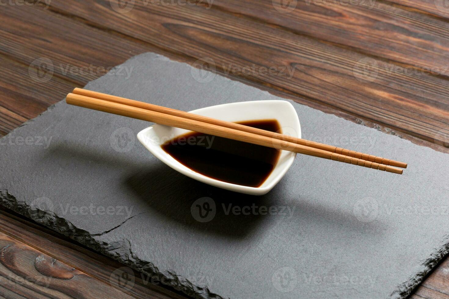 eetstokjes en soja saus Aan zwart steen bord, houten achtergrond foto