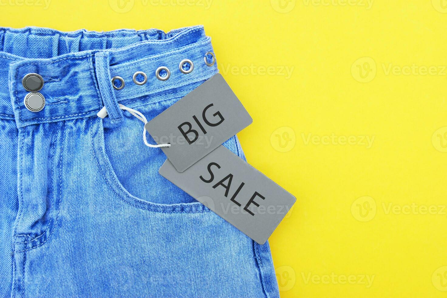 vlak leggen, detail van denim jeans met grijs etiket en opschrift groot uitverkoop Aan geel achtergrond. foto