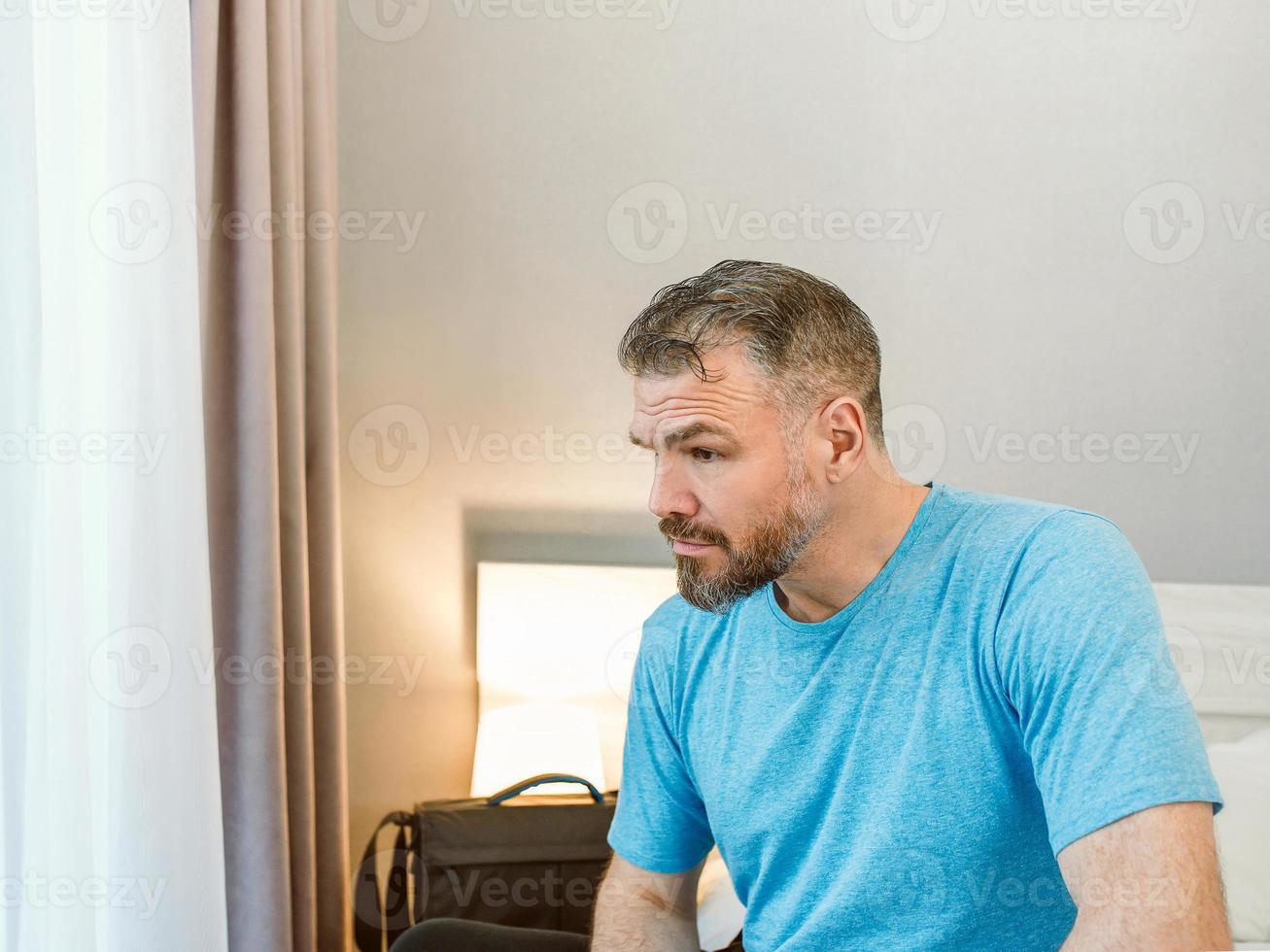 ongelukkige knappe man zit alleen op het bed in de slaapkamer. echtscheiding, slapeloosheid, depressie, problemen foto