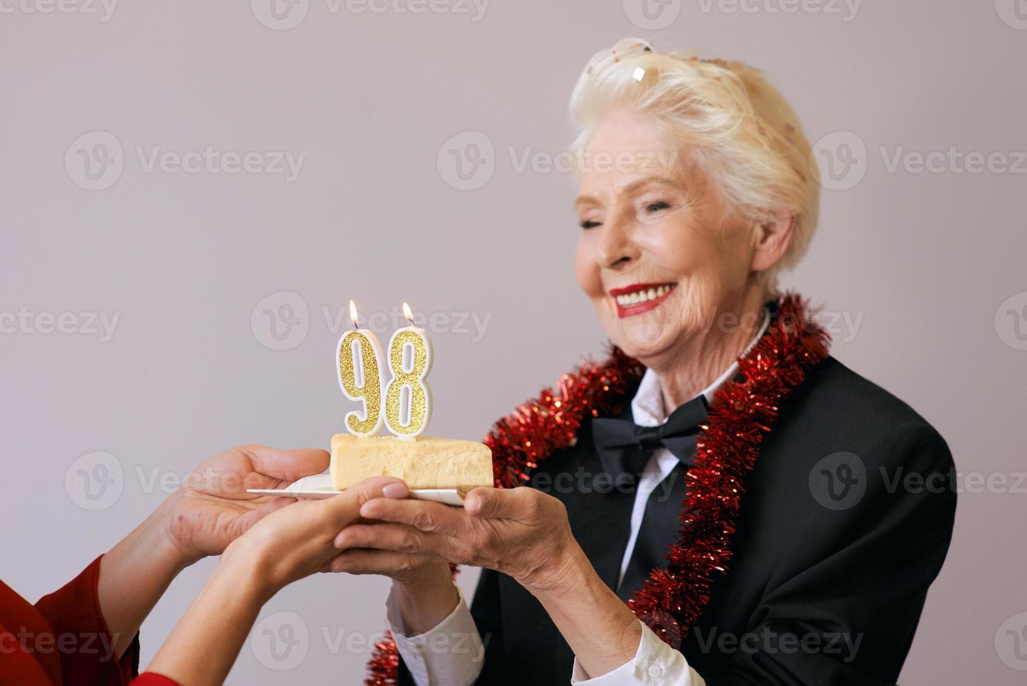 gelukkige vrolijke stijlvolle achtennegentig jaar oude vrouw in zwart pak viert haar verjaardag met taart. levensstijl, positief, mode, stijlconcept foto