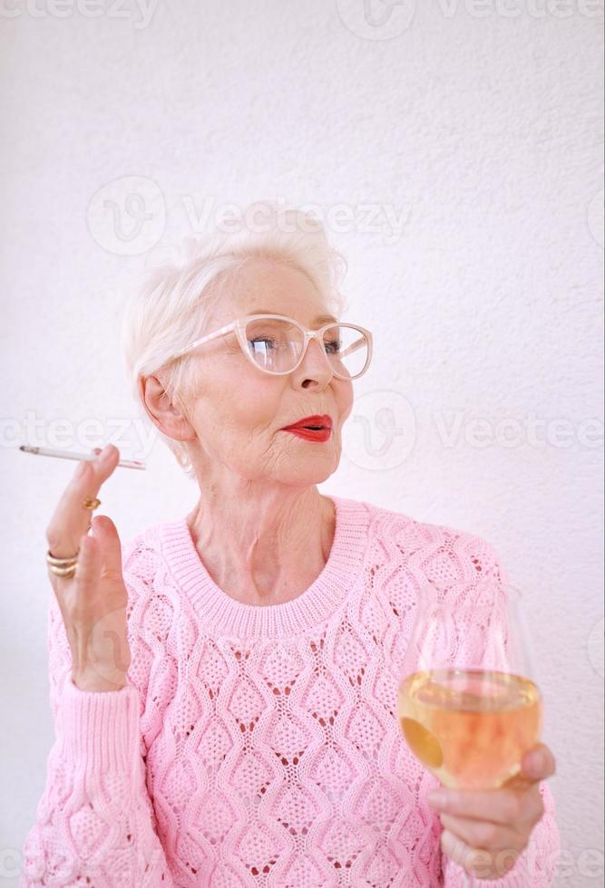 ouderwetse senior stijlvolle vrouw roken sigaret met glas witte wijn. slechte gewoonte, verslavingsconcept foto