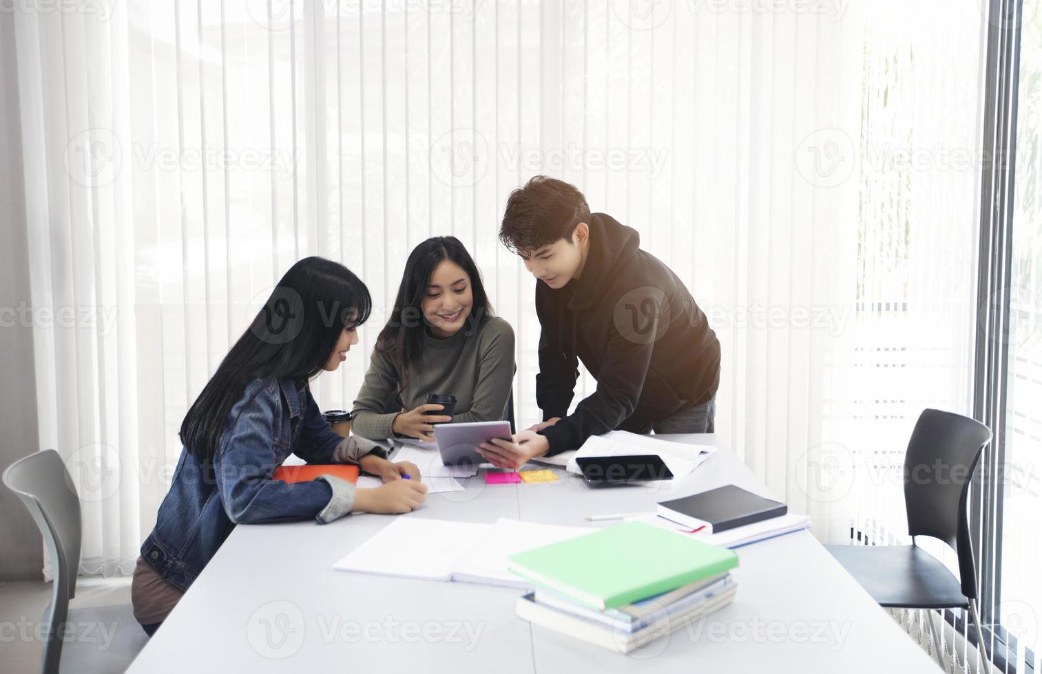 Groepsstudenten lachen en hebben plezier en het gebruik van een tablet helpt ook om ideeën te delen in het werk en het project. en bekijk ook het boek voor het examen foto