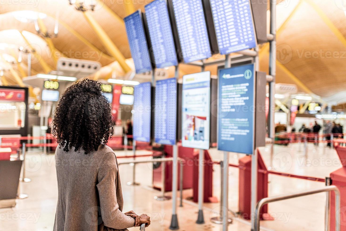 vrouw die met een koffer naar het informatiepaneel over de dienstregeling op de luchthaven kijkt foto