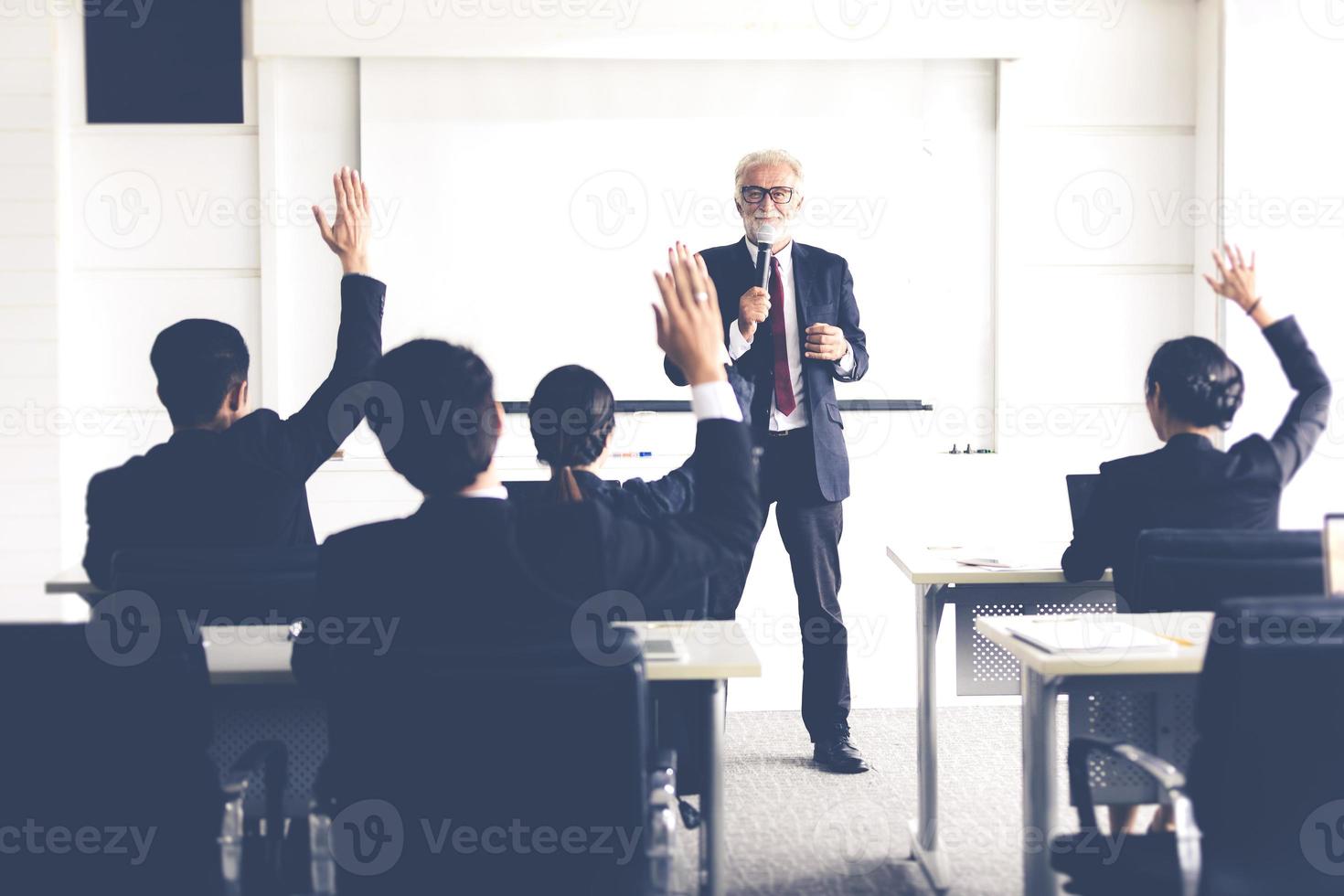 zakelijk publiek dat hand opsteekt terwijl zakenman in training spreekt voor advies met vergaderleider in vergaderruimte foto