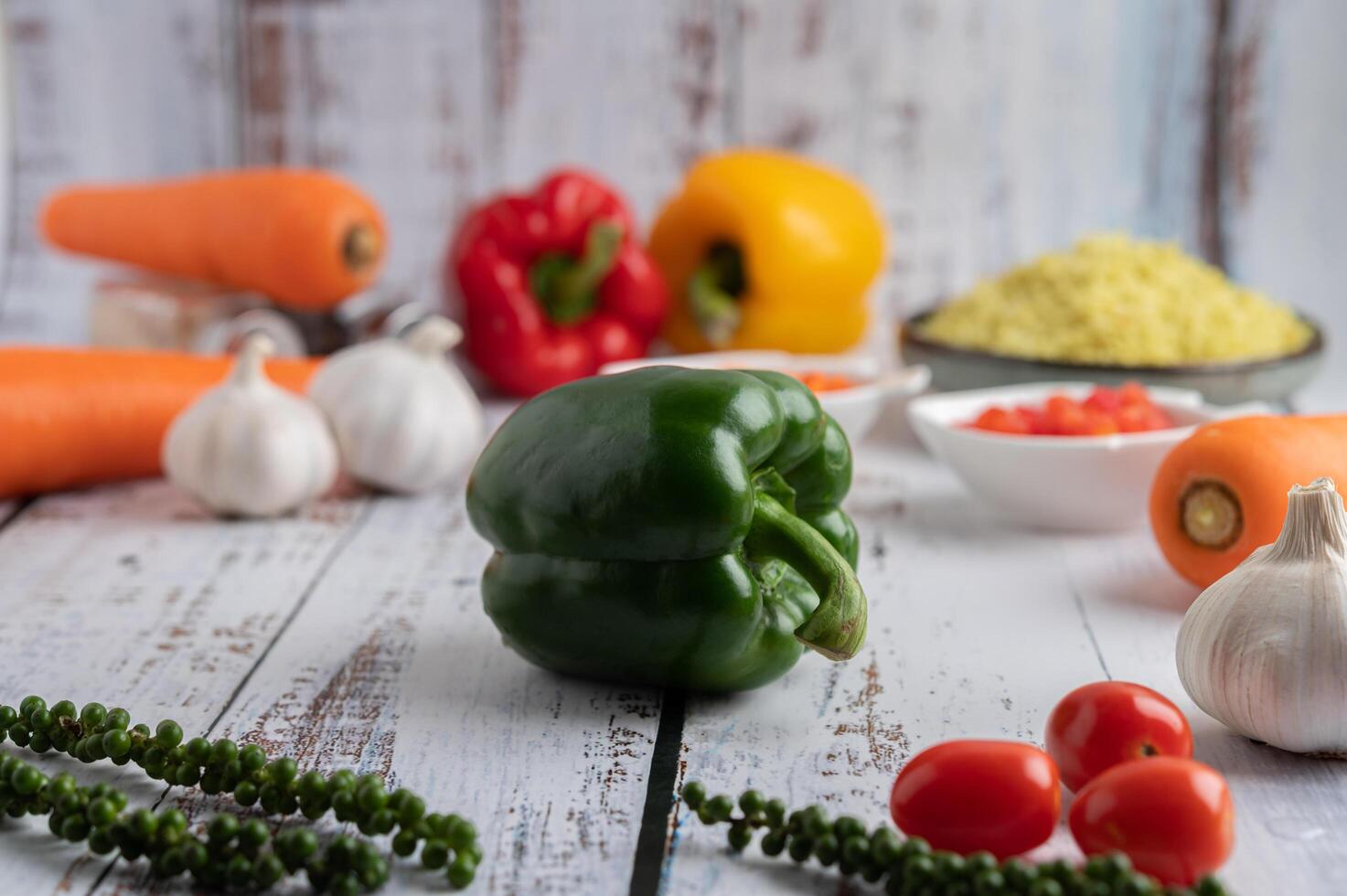 paprika, verse paprika, tomaten, knoflook en wortelen op een witte houten achtergrond. foto