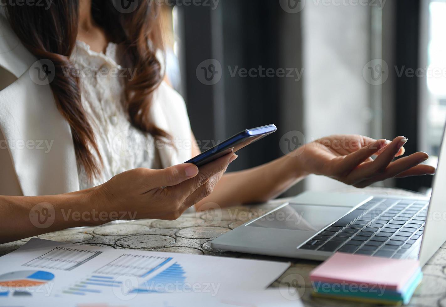 uitvoerende vrouwen gebruiken smartphone en laptop om de inkomsten samen te vatten. foto