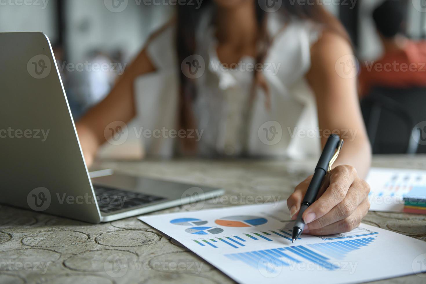 hand van een zakenvrouw houdt een pen vast die naar de grafiek wijst en een laptop gebruikt. foto
