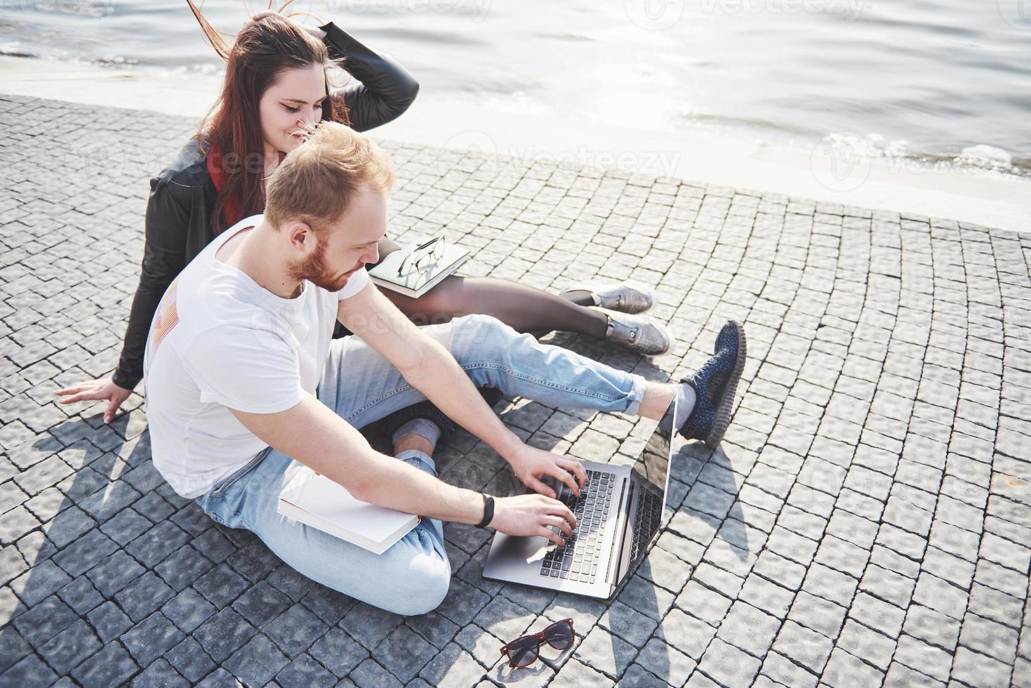 twee studenten, jongen en meisje, zitten buiten en genieten van een laptop, studeren buiten op een zonnige dag foto