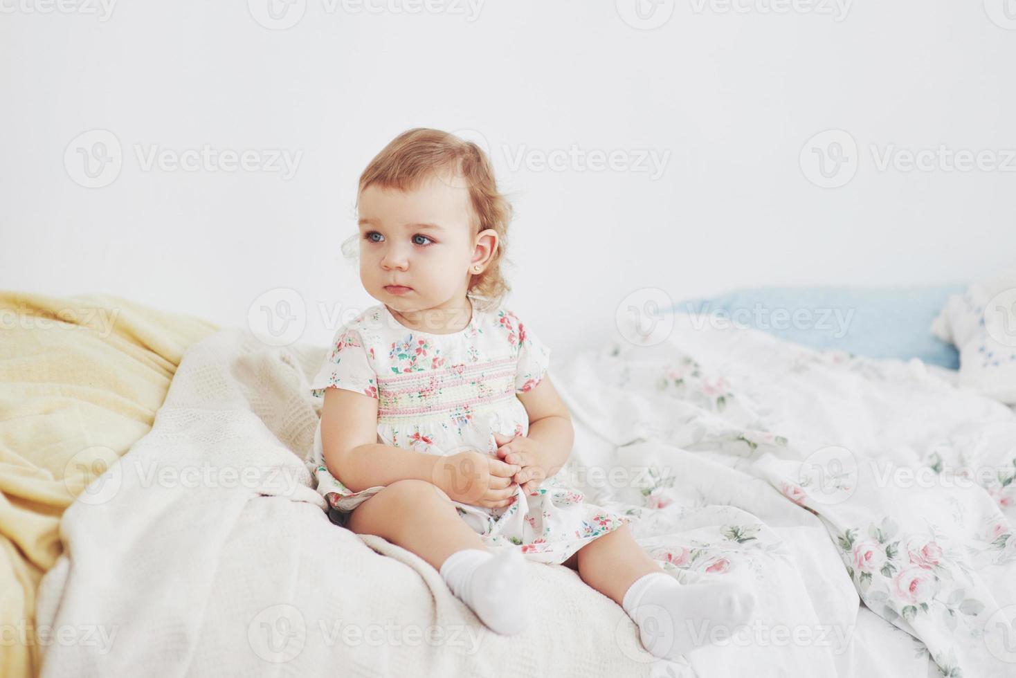 kindertijd concept. meisje van de baby in schattige jurk aanbrengen op bed spelen met speelgoed door het huis. witte vintage kinderkamer foto