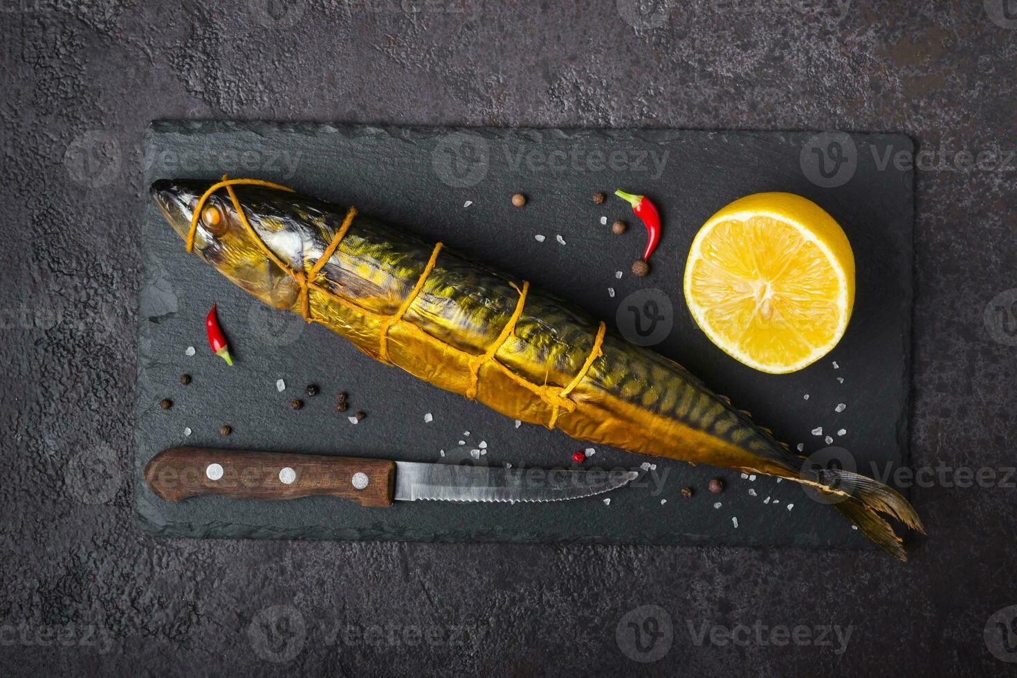 gerookt makreel vis, mes en citroen Aan zwart steen snijdend bord foto