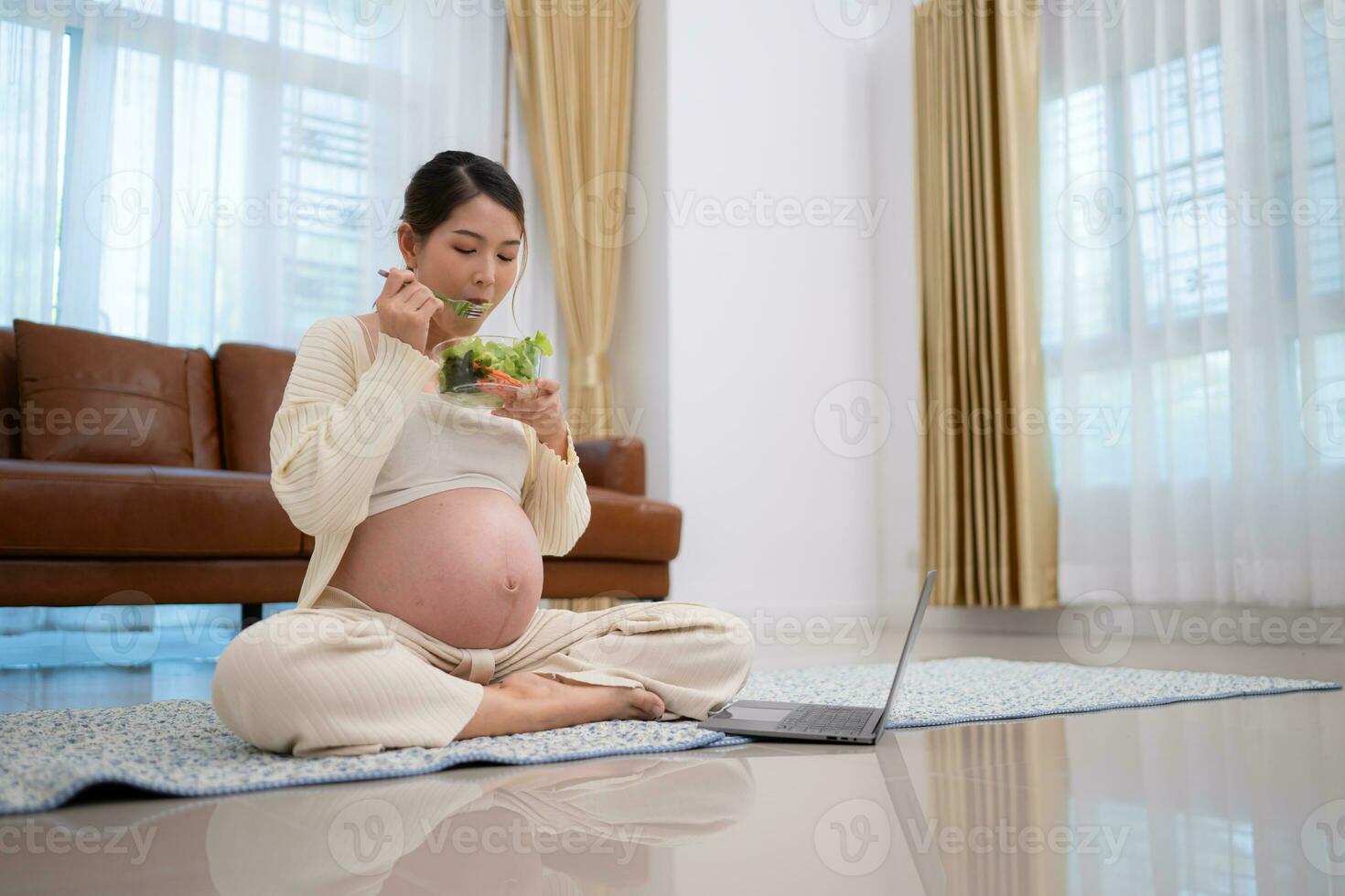 zwanger vrouw eet salade net zo een tussendoortje terwijl zittend Aan de verdieping van haar huis. foto