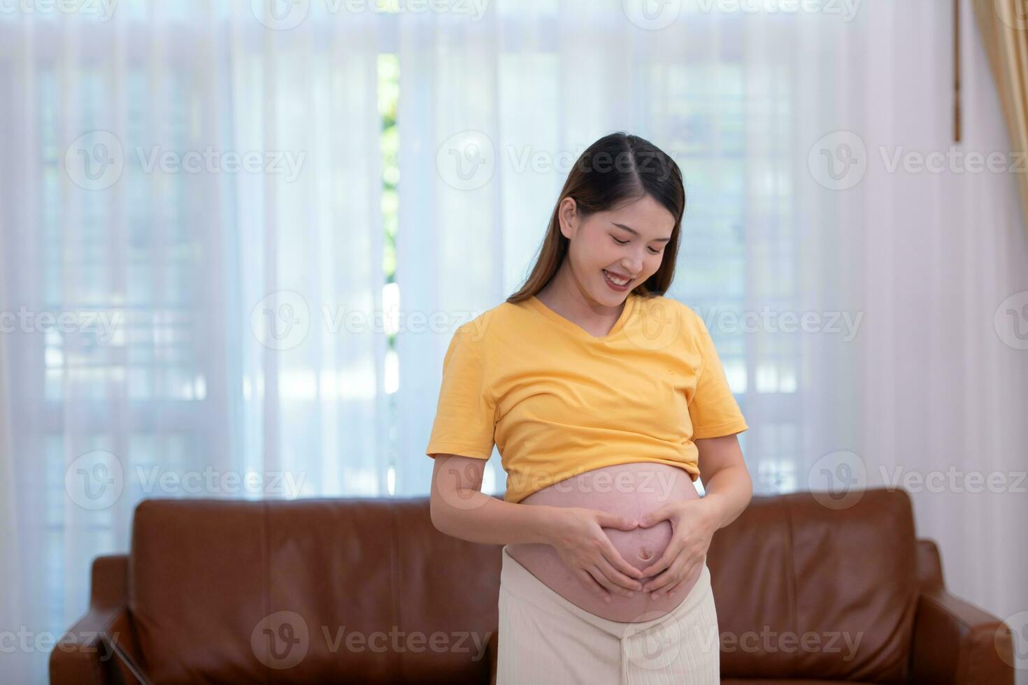 een zwanger vrouw voelt gelukkig Bij huis terwijl nemen zorg van haar baby in de baarmoeder. jong moeder tonen tekens van liefde naar haar baby in de baarmoeder foto