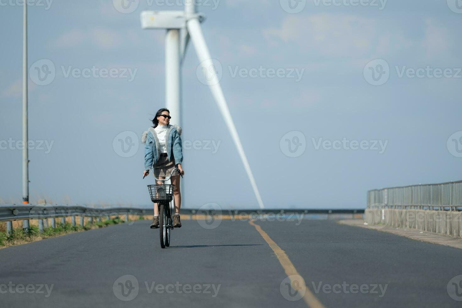 jong vrouw rijden een fiets Aan een weg in een windmolen. foto