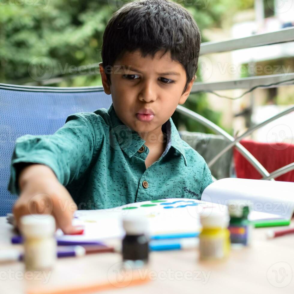 slim Indisch weinig jongen uitvoeren duim schilderij met verschillend kleurrijk water kleur uitrusting gedurende de zomer vakanties, schattig Indisch kind aan het doen kleurrijk duim schilderij tekening Aan houten tafel foto