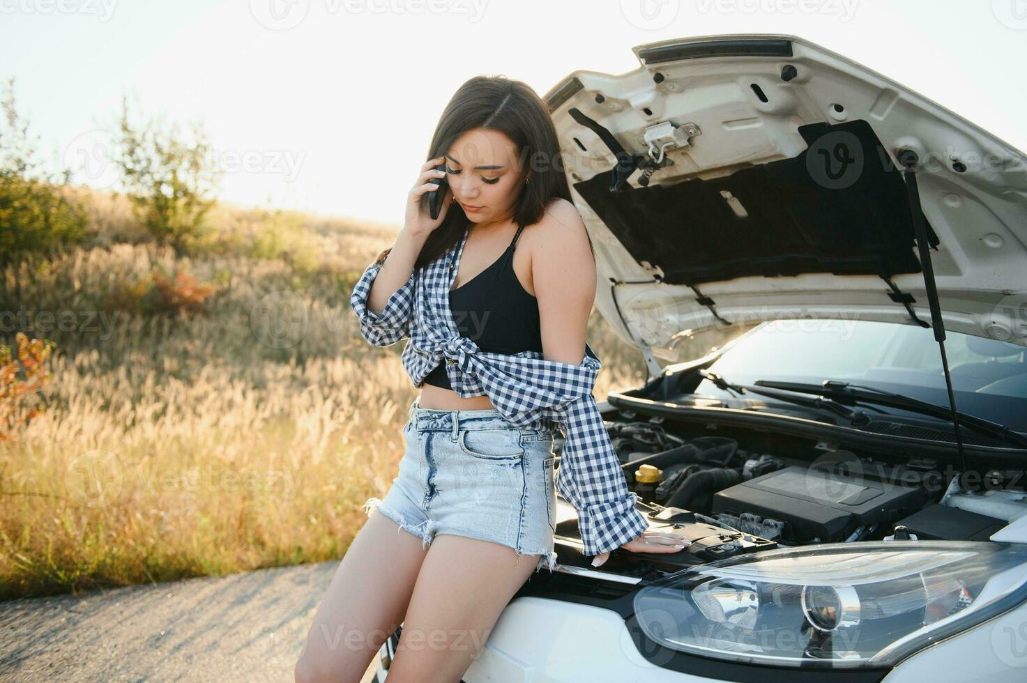 de jong meisje kapot gegaan de auto en ze geopend de kap en geprobeerd naar reparatie de auto Aan de weg. een vrouw oproepen Aan een smartphone met een auto evacuatie onderhoud foto