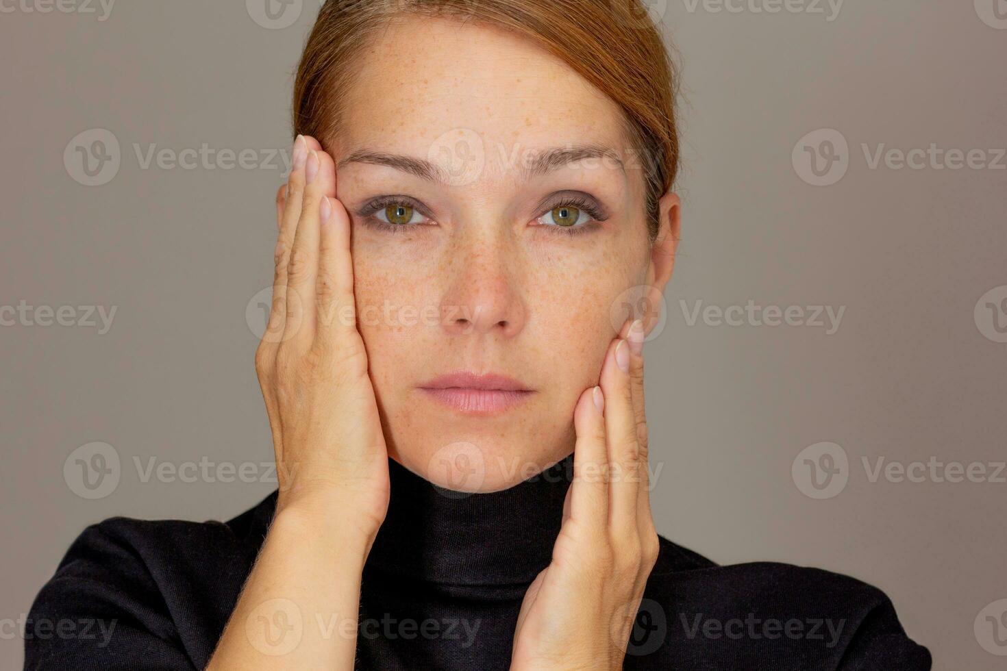 portret van Kaukasisch midden- oud vrouw van Jaren 40 op zoek Bij camera Holding palmen Aan wangen foto