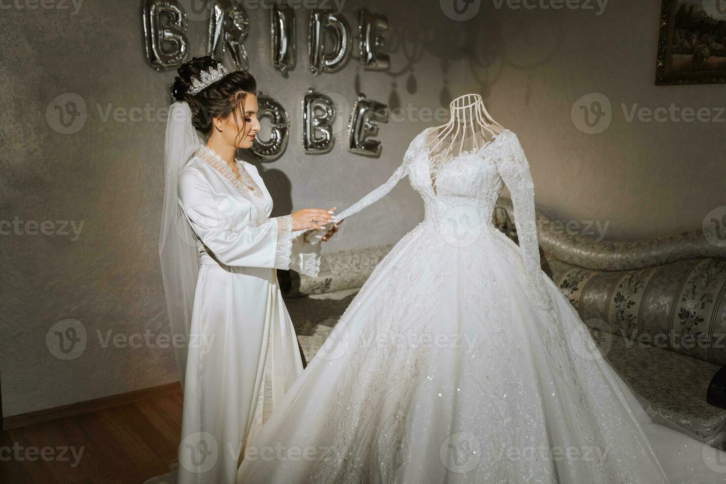 een brunette bruid in een satijn gewaad staat in de buurt de jurk. mooi haar- en verzinnen. bruiloft portret. oprecht glimlach. een mooi bruid in een gewaad poses De volgende naar haar jurk foto