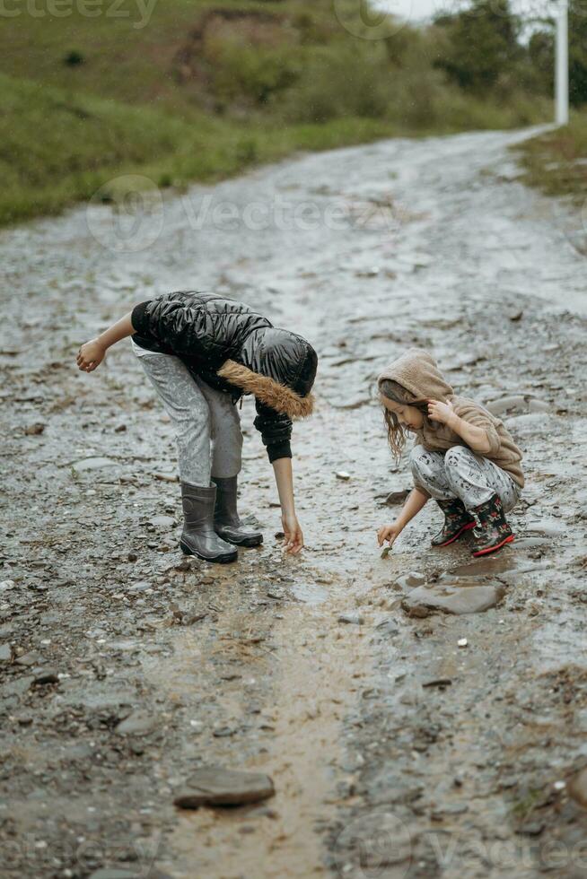 twee gelukkig weinig meisjes van Europese uiterlijk spelen in plassen gedurende regen in zomer. kinderen zijn spelen in de regen. kind spelen in natuur buitenshuis. de meisje geniet de regen. foto