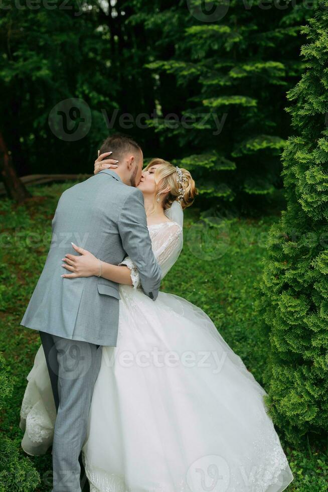 portret van de bruid en bruidegom staand tegen de achtergrond van groen bomen, de bruidegom zetten Aan de bruid bruiloft ring. elegant bruidegom. mode en stijl. foto