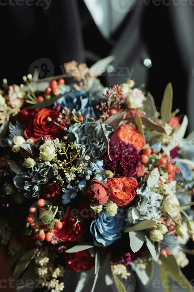 mooi bruiloft boeket met verschillend bloemen in de handen. rustiek bruiloft boeket met rood en blauw rozen en wit anjers. detailopname. kant visie foto