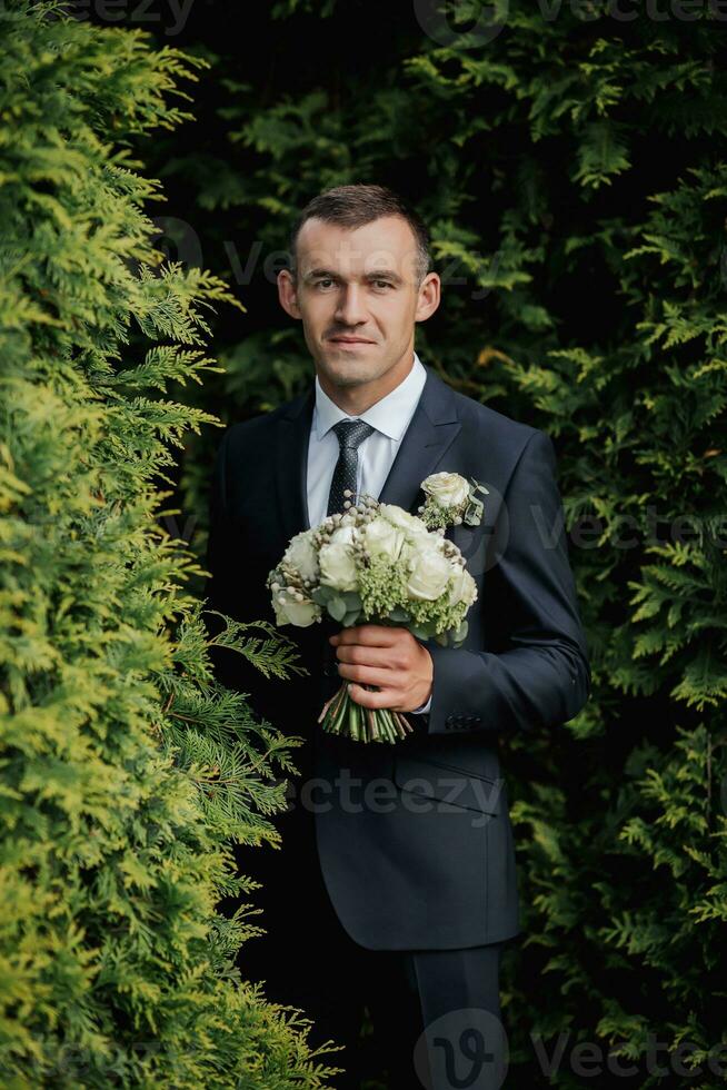 een Mens in een zwart pak poses in natuur met een boeket. een elegant horloge. Mannen stijl. mode. bedrijf. foto