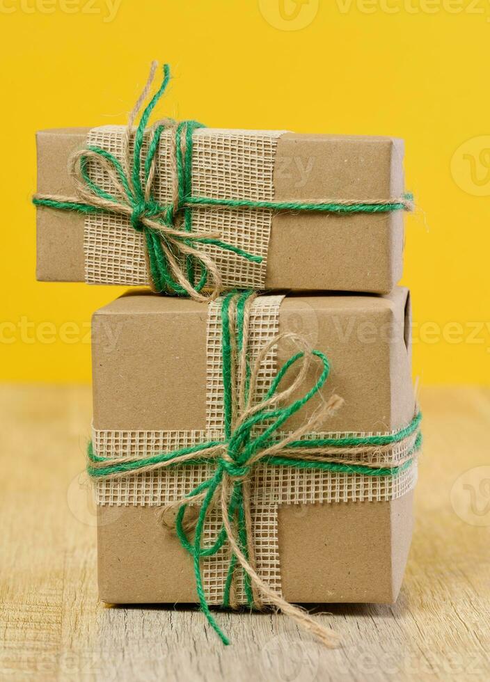 de doos is Ingepakt in bruin ambacht papier en gebonden met een touw Aan een beige achtergrond, geschenk foto